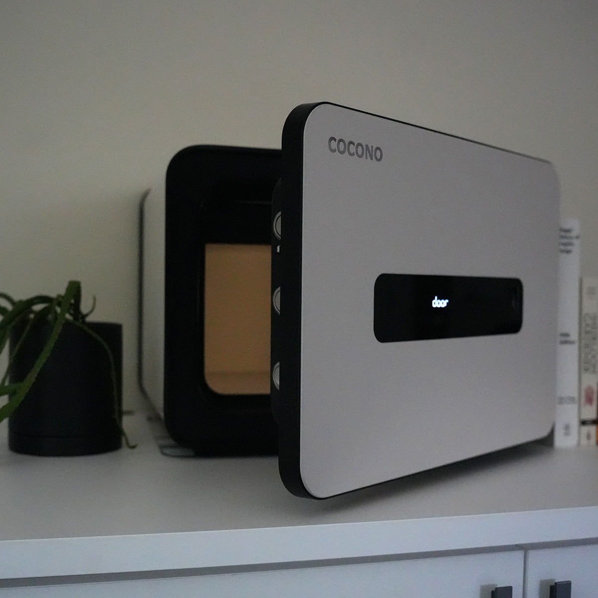 Cocono 20 small safe in Ivory with door open, next to a plant.