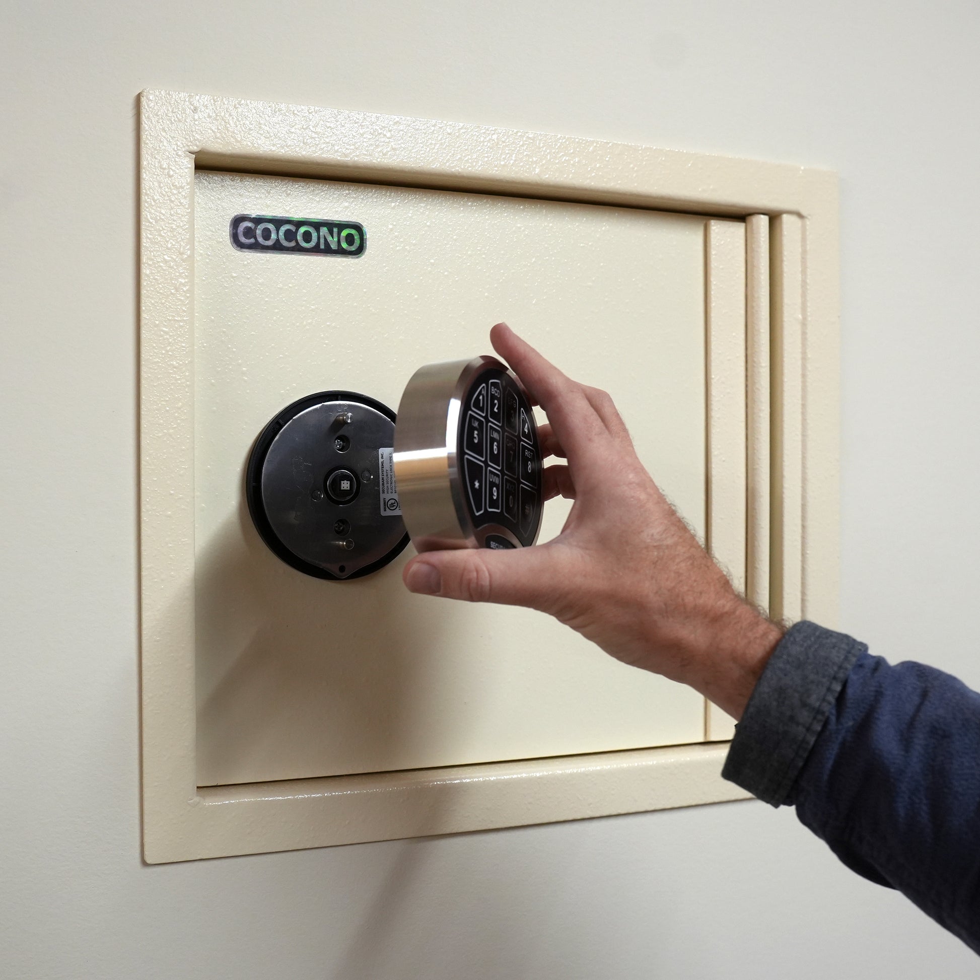 Cocono wall safe hidden in wall, shown in Ivory with U.L. electronic lock being removed for extra security